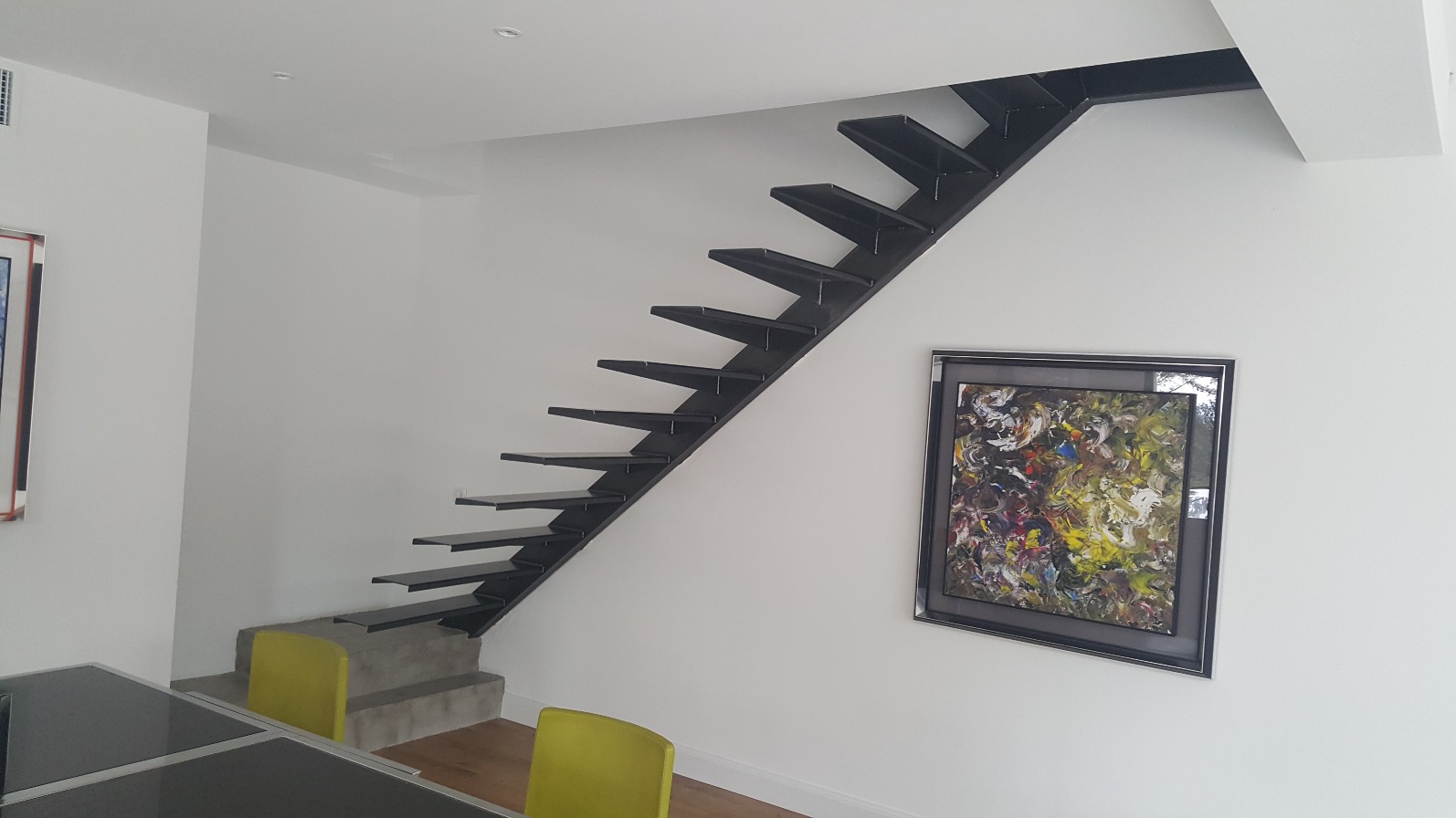 Escalier moderne en fer forgé intégré au mur, avec des marches discrètes qui semblent flotter, créant une illusion de légèreté et de sophistication architecturale