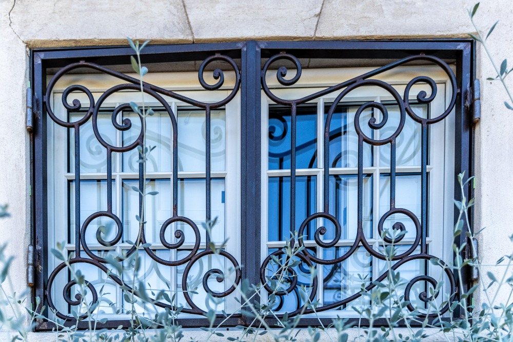 une grille de défense robuste, conçue spécifiquement pour une porte double battant. Fabriquée en fer forgé, elle offre à la fois sécurité et esthétique, avec des motifs décoratifs qui s'harmonisent avec l'architecture environnante.